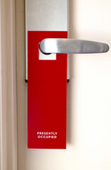 Red sign hanging on door that says Presently Occupied