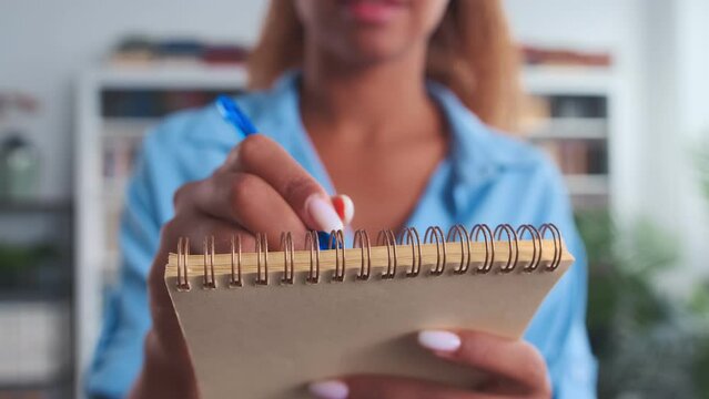 Closeup of hand African American woman with pen making notes in notepad making shopping list or fixing work schedule and plan of work meetings so as not to forget anything standing in office room