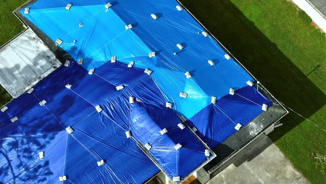 Top view of leaking house roof covered with protective tarp sheets against rain water leaks until replacement of asphalt shingles. Damage of building rooftop as aftermath of hurricane Ian in Florida