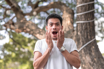 A Southeast Asian guy holds his hands in front of his mouth with a shocked or surprised expression on his face upon hearing the biggest revelation.