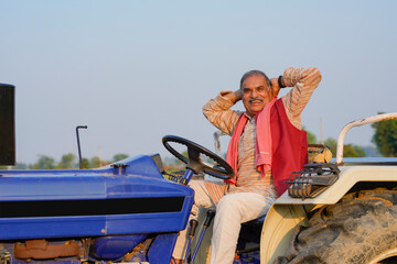 Indian farmer sitting on tractor and giving expression at agriculture field. © Niks Ads