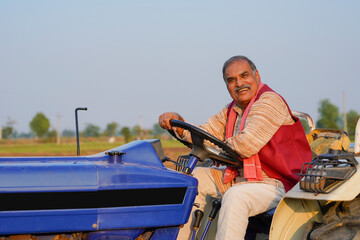 Indian farmer sitting on tractor and giving expression at agriculture field. © Niks Ads