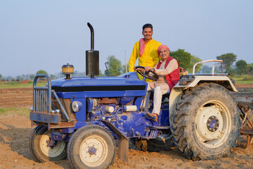 Obraz premium Young indian farmer with father sitting on new tractor at field.