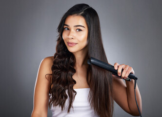 Portrait, woman and hair straightener for care, natural beauty or treatment on grey studio background. Female, girl and salon equipment for luxury, ironing hair style and grooming routine for styling