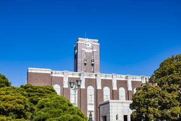 Fototapeta premium Kyoto University Clock Tower Centennial Hall and the Camphor Tree under the clear sky. This tower had been loved as the university's symbol. 