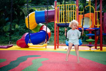 Fototapeta na wymiar Child on a swing in summer. Emotions on the playground on a swing. Blonde curly girl is resting.