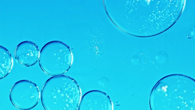 Liquid texture with burst drops on light blue background. Gel cosmetic with molecule bubbles. Macro shot of air bubbles. Skincare gel ingredients and water for its commercial.