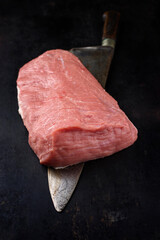 Raw cap of rump calf offered with a knife as close-up on a black board with copy space