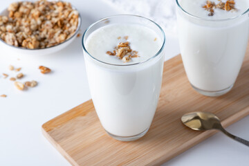 Kefir, buttermilk or yogurt with granola. Yogurt in glass on white wooden background. Probiotic cold fermented dairy drink. Gut health, fermented products, healthy gut flora concept. Copy space
