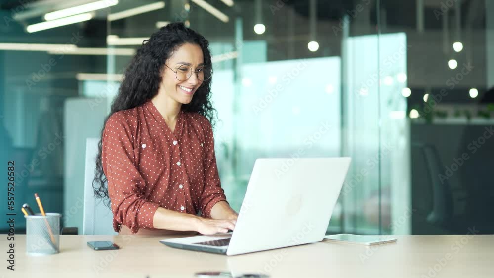 Wall mural curly brunette employee works in a modern office at workplace at a laptop computer focused and confi