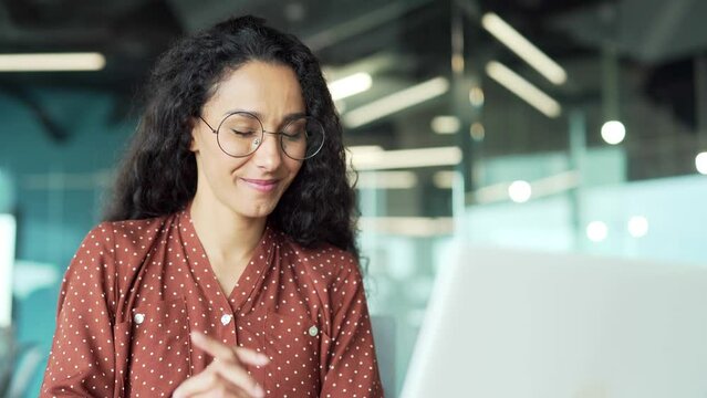 Close-up young beautiful business woman with curly hair and glasses Hispanic employee talking on video call using laptop for remote communication and meeting conference in a modern office Closeup