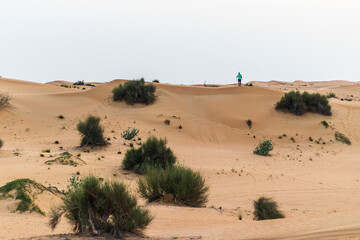Young boy walks around sand dunes in the desert. People