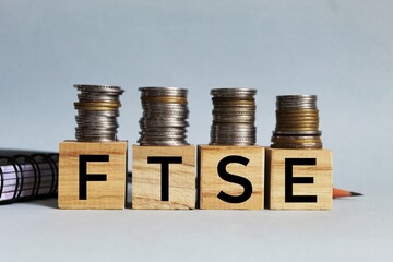 FTSE concept, Financial Times Stock Exchange Group - acronym on wooden cubes on coins on a white background. Business concept