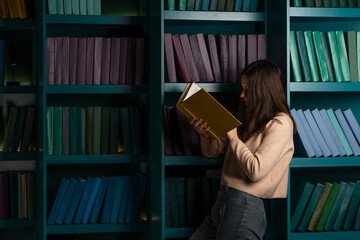 Read books, fiction and educational literature, concept. A young woman with an open book on the background of bookshelves.