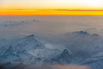 The Alps at sunrise with light fog and orange sky.