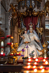 Fototapeta na wymiar Une vierge marie en majesté avec l'enfant jesus dans les bras derriere des rangées de bougies allumées 