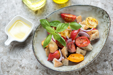 Bowl with panzanella or italian tomato and bread salad, elevated view on a light-brown granite background