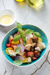 Tuscan-style tomato and bread salad or panzanella, vertical shot on a light-beige marble background