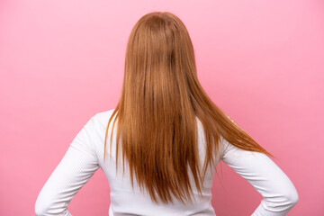 Young redhead woman isolated on pink background in back position