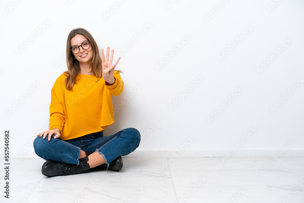 Wall mural Young caucasian woman sitting on the floor isolated on white background happy and counting four with fingers