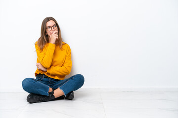 Young caucasian woman sitting on the floor isolated on white background having doubts and with...