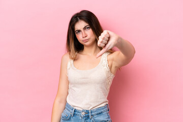 Young caucasian woman isolated on pink background showing thumb down with negative expression