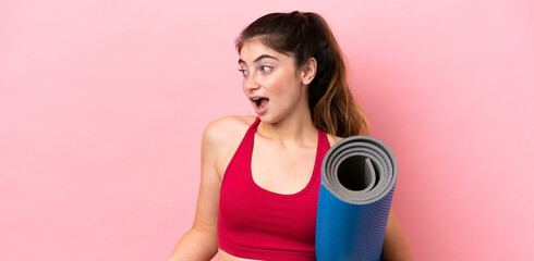 Young sport woman going to yoga classes while holding a mat with surprise expression while looking...