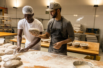 Bakers school, master baker kneading bread dough on the table with flour, teaching the technique to his apprentice  - obrazy, fototapety, plakaty