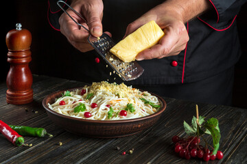 The cook adds hard cheese to a plate of spaghetti. Working environment in the hotel kitchen