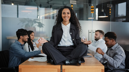 Smiling mindfulness businesswoman happy leader woman sitting at table in lotus position meditating...