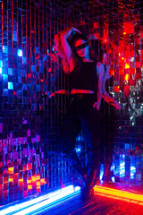 Portrait of a caucasian woman in sunglasses in neon light against a mirror wall. 