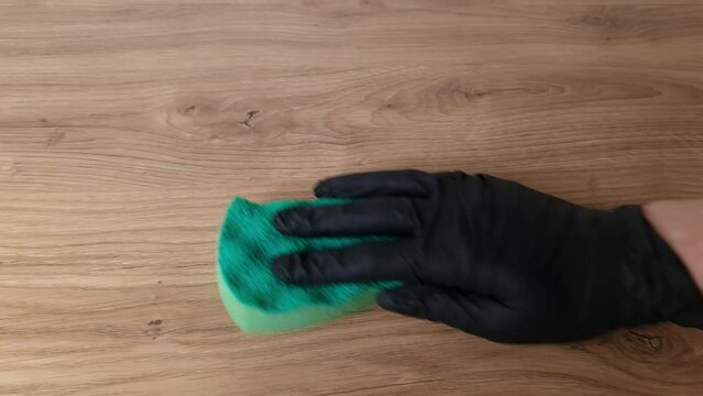 Female hand in black rubber protective glove wiping wooden surface from dust with green sponge. Commercial cleaning company, disinfection, general or regular cleanup concept
