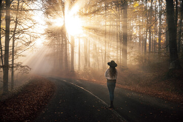 Young  woman standing in the rays of the morning sun in a leafy autumn forest and enjoying the magical view. 