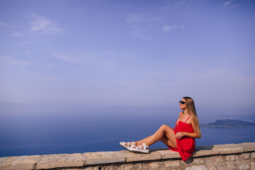 Tourist woman in red dress enjoying view on Adriatic sea on sunny day