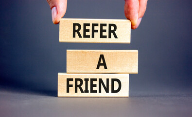 Refer a friend symbol. Concept words Refer a friend on wooden blocks on a beautiful grey table grey background. Businessman hand. Business and refer a friend concept. Copy space.