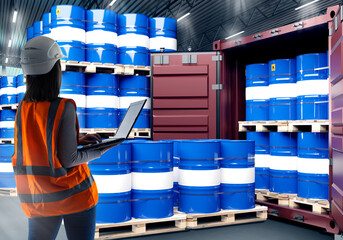 Oil logistics. Woman with laptop in warehouse. Blue barrels near container. Barrels of oil on...