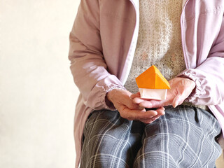 折り紙の家を持つ高齢女性の手