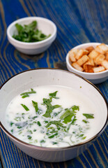 yogurt soup with herbs and crackers on a blue wooden table