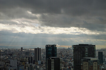 Fototapeta na wymiar Overhead view of Osaka's Umeda area from a hill on a cloudy day, sunlight shining through a gap in the clouds.