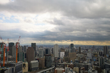 Overhead view of Osaka's Umeda area from a hill on a cloudy day, sunlight shining through a gap in the clouds.