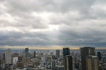 Fototapeta na wymiar Overhead view of Osaka's Umeda area from a hill on a cloudy day, sunlight shining through a gap in the clouds.