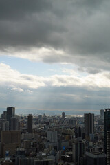 Overhead view of Osaka's Umeda area from a hill on a cloudy day, sunlight shining through a gap in the clouds.