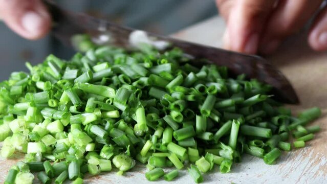 Close Up of hand holding knife cutting green onions, chives. Sliced ​​with a knife on a wooden cutting board. Finely chop fresh green onions.