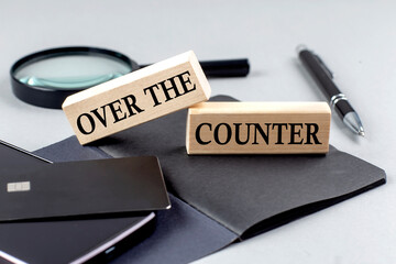 OVER THE COUNTER text on wooden block on black notebook , business concept