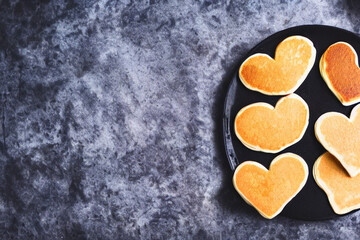 Fototapeta na wymiar Heart shaped pancakes on black background with copy space for text 