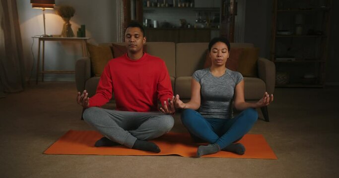 Latin couple meditates together on orange mat in apartment