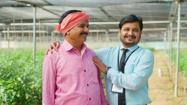 happy smiling supportive banker with Indian farmer standing at green house by looking at camera - conept of expertise, assurance and cooperation.