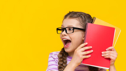 Surprised little schoolgirl on an isolated background. A girl with textbooks and notebooks in glasses.
