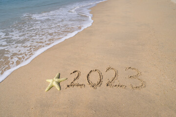 2023 hand written with starfish in sand on a beautiful beach