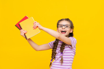 The girl shows her notebooks and rejoices. a child on a yellow background. A little girl with glasses.